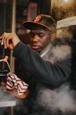 A man wearing a cap operates machinery, surrounded by steam or smoke, while holding a striped cloth.