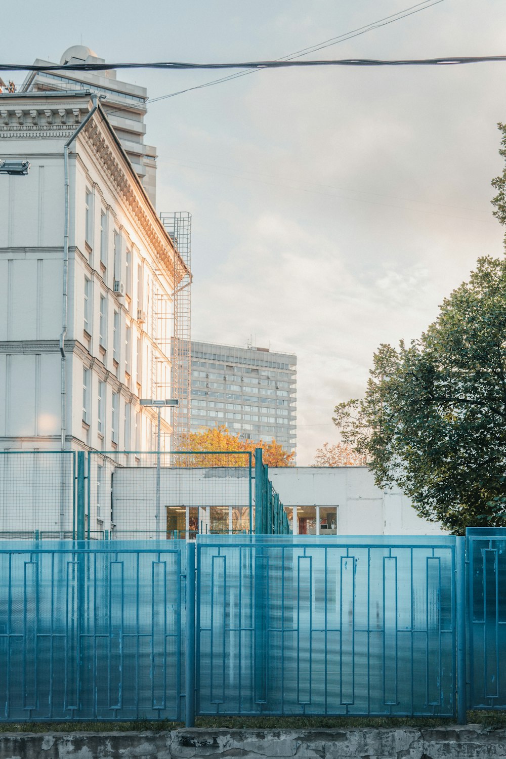 a tall white building sitting next to a blue fence