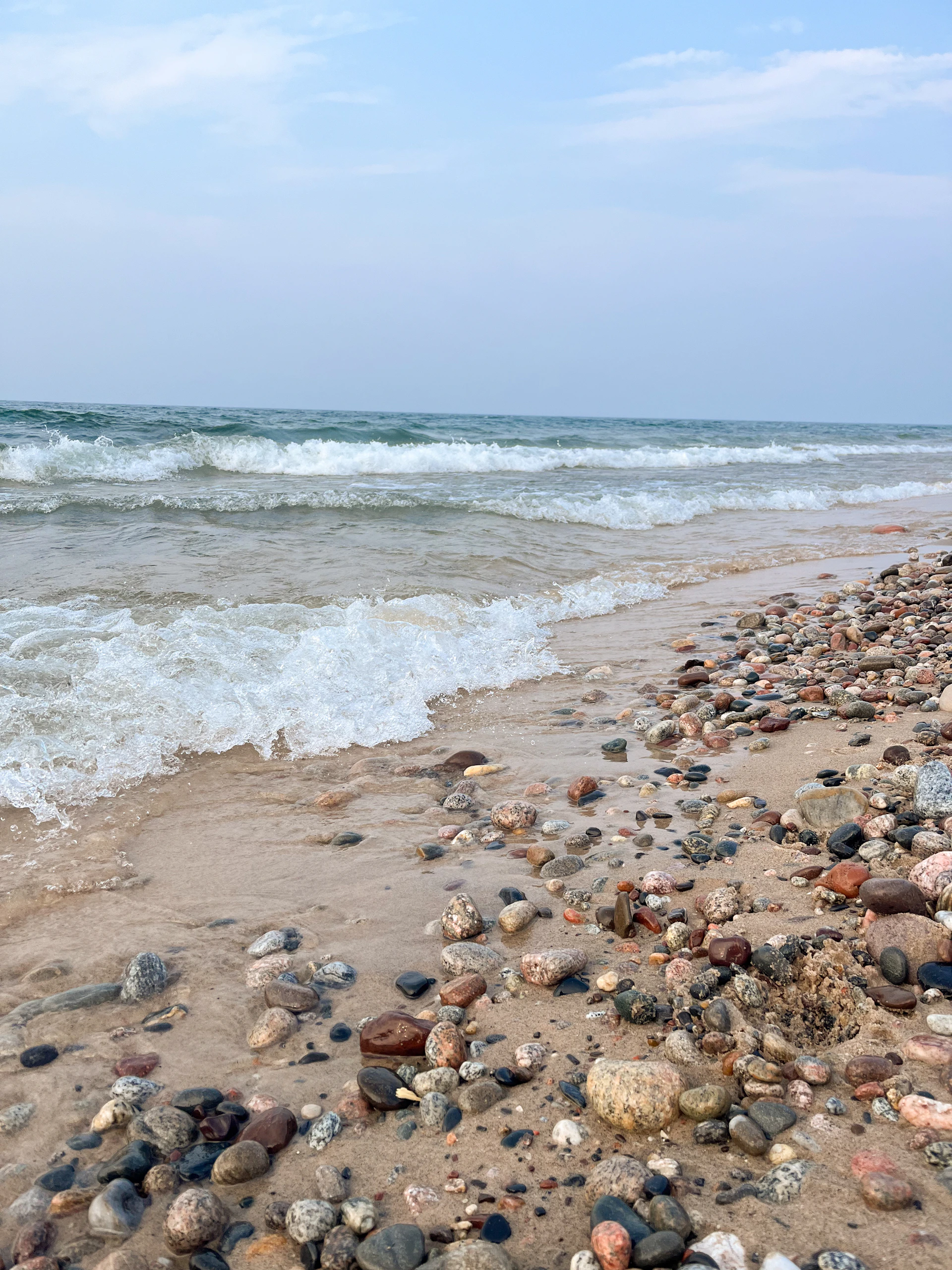A calm beach scene with gentle waves lapping against smooth, colorful stones under a pastel sky.