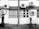 A building exterior with several air conditioning units attached to the walls. The windows have metal bars and there's noticeable black staining below some units. A metal grill is leaning against the wall near the bottom.