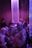 A dimly lit environment with a group of people engaging in a lively social gathering. The lighting casts a purple and blue hue over the scene with shimmering vertical strings hanging from the ceiling, creating a dynamic and energetic atmosphere.