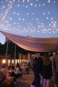 Guests mingling happily on a charming outdoor terrace with string lights glowing as evening approaches.