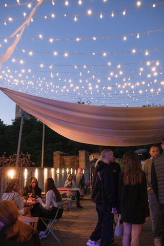 Guests mingling happily on a charming outdoor terrace with string lights glowing as evening approaches.