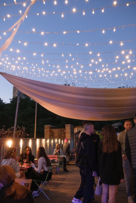 A cozy rooftop gathering at dusk with people engaged in deep conversation under warm string lights.