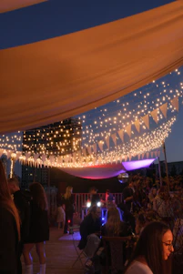 A vibrant outdoor party setup with elegant furniture and colorful decorations under string lights at dusk.
