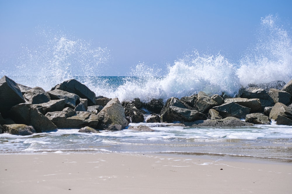 a wave crashes over rocks on the beach