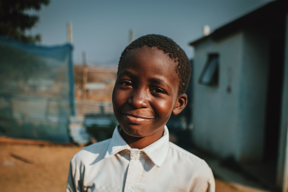 a young boy in a white shirt smiles at the camera