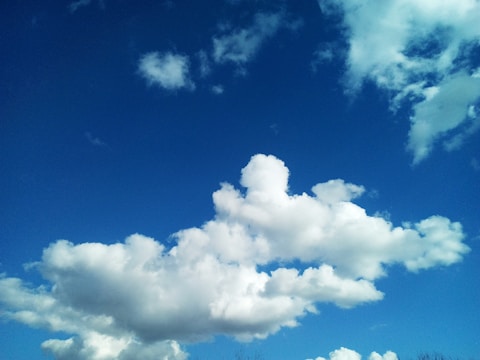 Bright blue sky filled with large fluffy white clouds forming various shapes. The clouds have soft edges and are scattered across the sky, providing a sense of depth and movement.