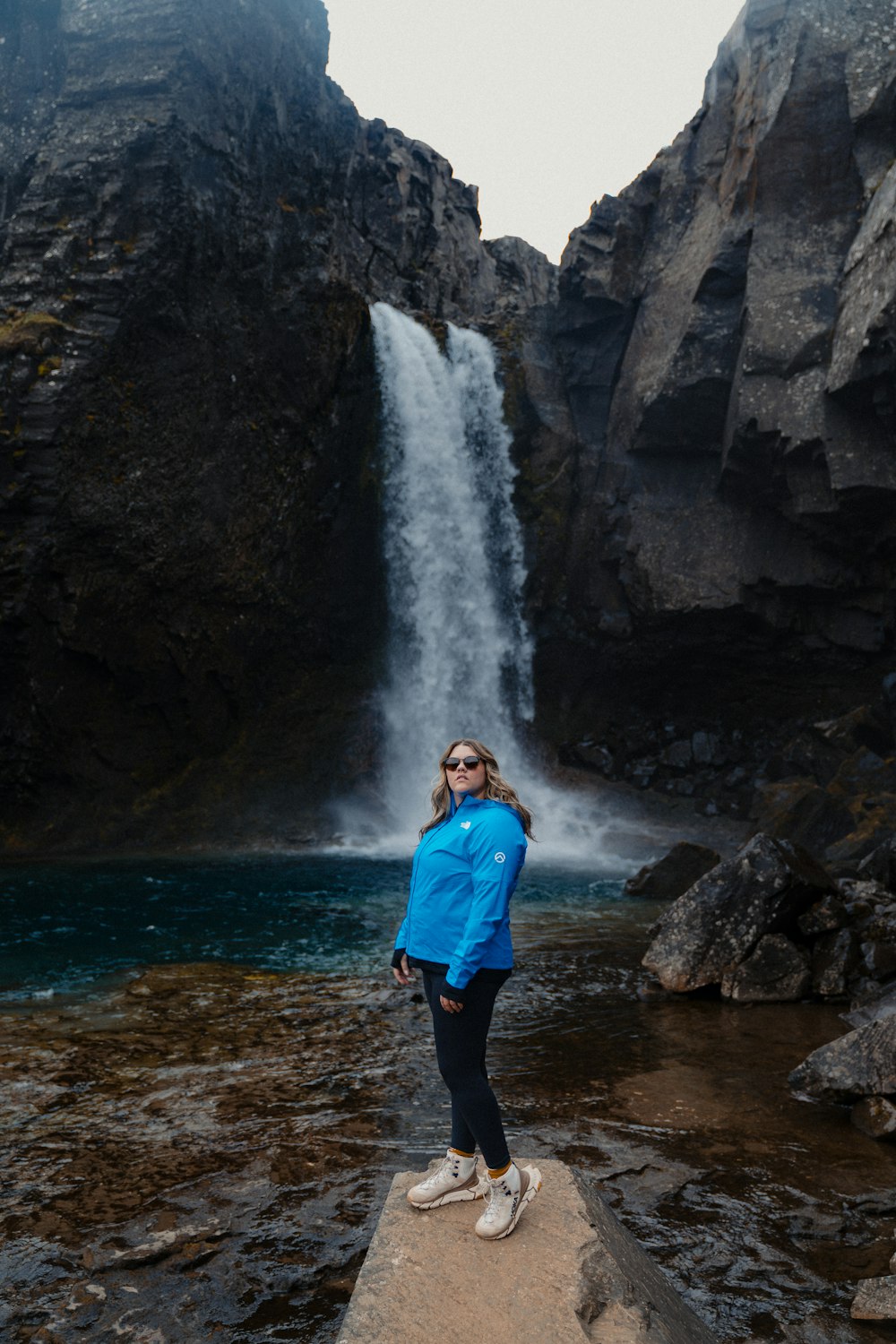 Una mujer parada en una roca frente a una cascada