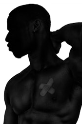 Silhouette of a muscular man with his hand placed behind his neck, revealing a bandage in an X shape on his chest.