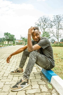 Casual pants styled with a relaxed shirt and sneakers, set in a sunny outdoor park setting with greenery.