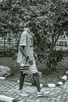 A laid-back individual walking through a park, sporting a Lazy Legend Club tote bag and sneakers.