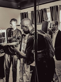 A group of people are in a room with professional camera equipment, engaged in what appears to be a filming or photography session. Various individuals hold cameras and other gear, focusing intently on their work.