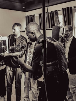 A group of people are in a room with professional camera equipment, engaged in what appears to be a filming or photography session. Various individuals hold cameras and other gear, focusing intently on their work.