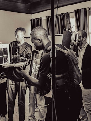 A group of people are in a room with professional camera equipment, engaged in what appears to be a filming or photography session. Various individuals hold cameras and other gear, focusing intently on their work.