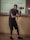 A person in a dark outfit is holding a camera gimbal while standing in a room with a tiled floor. Behind them, a projection on the wall displays equations and textual information. The individual is focused on capturing video or pictures, and the lighting suggests an indoor setting.