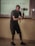 A person in a dark outfit is holding a camera gimbal while standing in a room with a tiled floor. Behind them, a projection on the wall displays equations and textual information. The individual is focused on capturing video or pictures, and the lighting suggests an indoor setting.