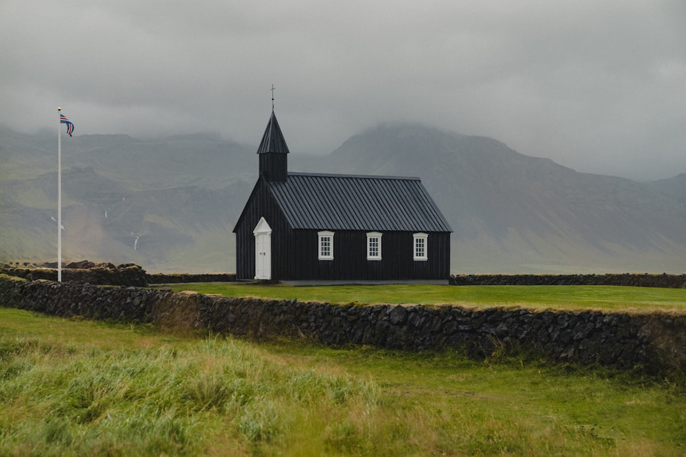 Una pequeña iglesia negra con un campanario en un campo cubierto de hierba
