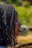 A side profile of a person with braided hair, set against a blurred, natural background with green and earthy tones.