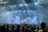A panoramic view of the concert crowd illuminated by stage lights.