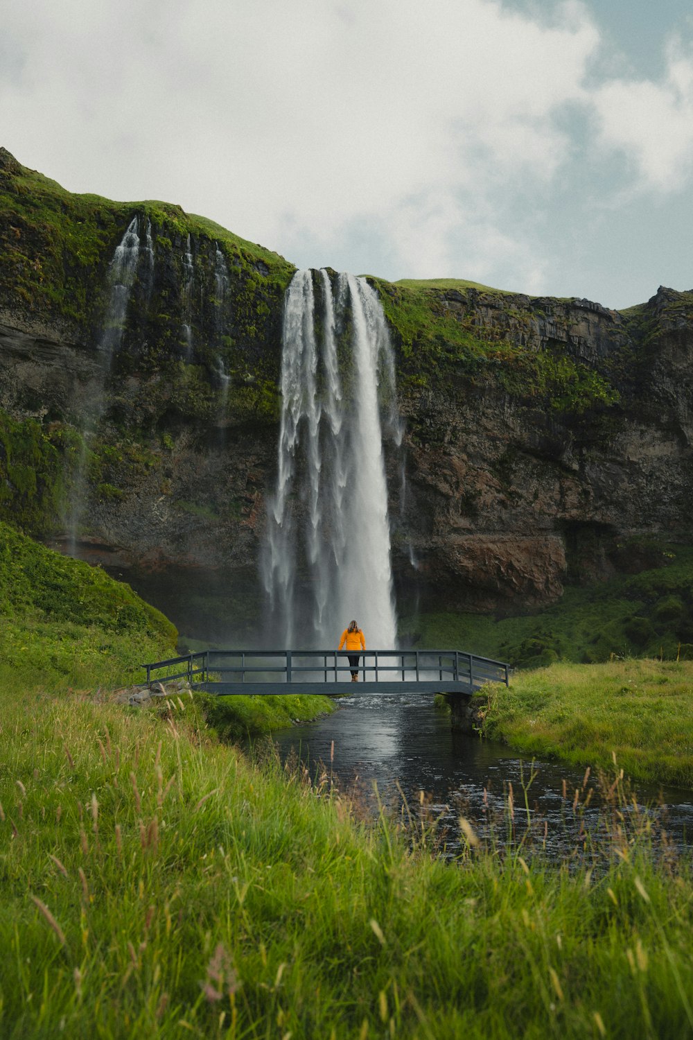 a person standing on a bridge in front of a waterfall