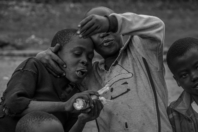 Three children are closely interacting, with two of them engaged in playful laughter. One child has an arm around another, and they are sharing a piece of corn. The third child looks slightly away from the camera. The scene conveys a sense of camaraderie and joy.