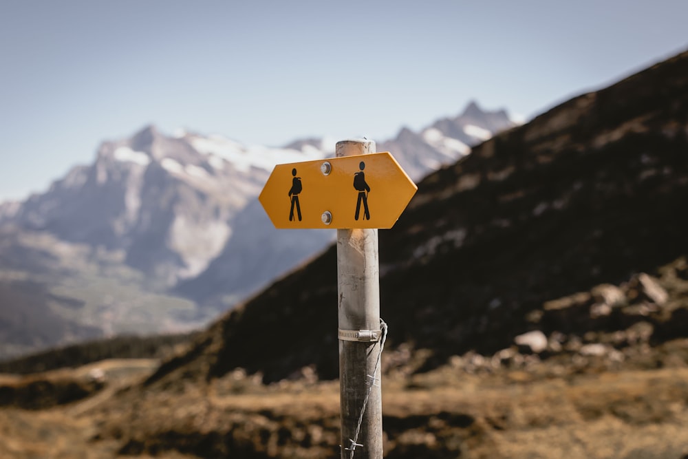 Un letrero amarillo en un poste con montañas en el fondo