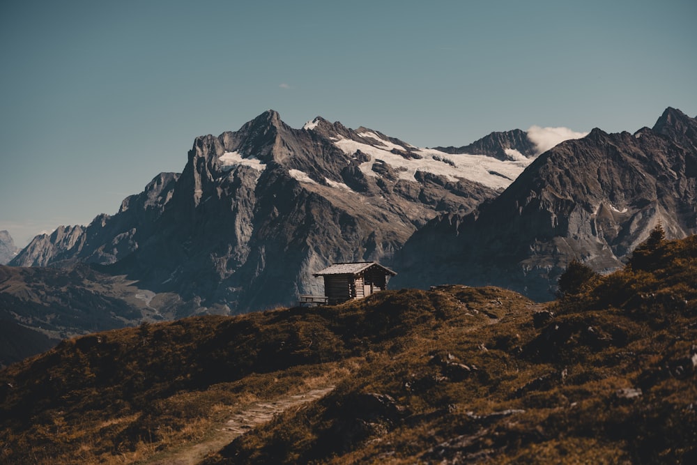 a small cabin on a grassy hill with mountains in the background