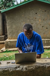 A builder using a laptop outdoors with construction materials in the background.