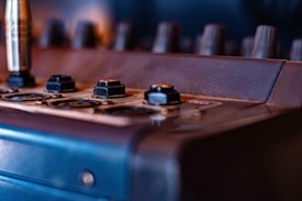 A close-up view of an audio mixing board with visible knobs and connector ports. The surface appears slightly worn, and the lighting casts a warm glow across the equipment.