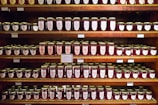 Rows of neatly labeled jam jars on wooden shelves in a cozy workshop.
