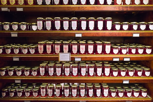Rows of glass jars filled with colorful fruit jams, labeled and ready for sale.