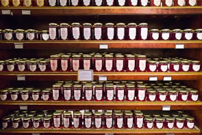 Rows of neatly labeled jam jars on wooden shelves in a cozy workshop.