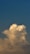 A large, fluffy cloud with hints of sunlight is set against a backdrop of a gradient blue sky, transitioning from deeper tones at the top to lighter towards the bottom.