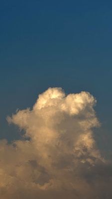 A large, fluffy cloud with hints of sunlight is set against a backdrop of a gradient blue sky, transitioning from deeper tones at the top to lighter towards the bottom.