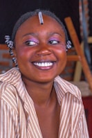 A joyful client showing off a vibrant, creative hairstyle and bold makeup for a special event.