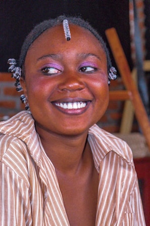 A joyful client showing off a vibrant, creative hairstyle and bold makeup for a special event.