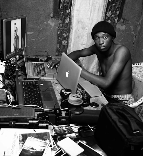 A candid photo of Ram Charan Singh working on his laptop surrounded by tech gadgets and camera equipment.