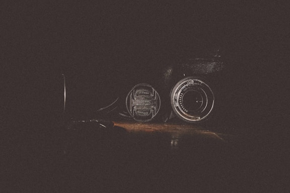 A sleek camera lens resting on a polished wooden table, softly lit to highlight its details.