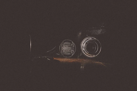 A sleek, moody studio shot of a film camera lens reflecting a golden-hued scene, set against a dark charcoal background.