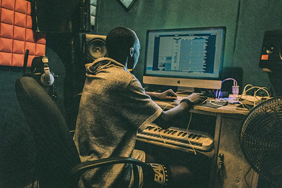 A composer working in a studio surrounded by screens showing film scenes.