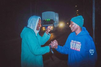 A friendly handshake between buyer and seller beside a shiny used car on a sunny day.