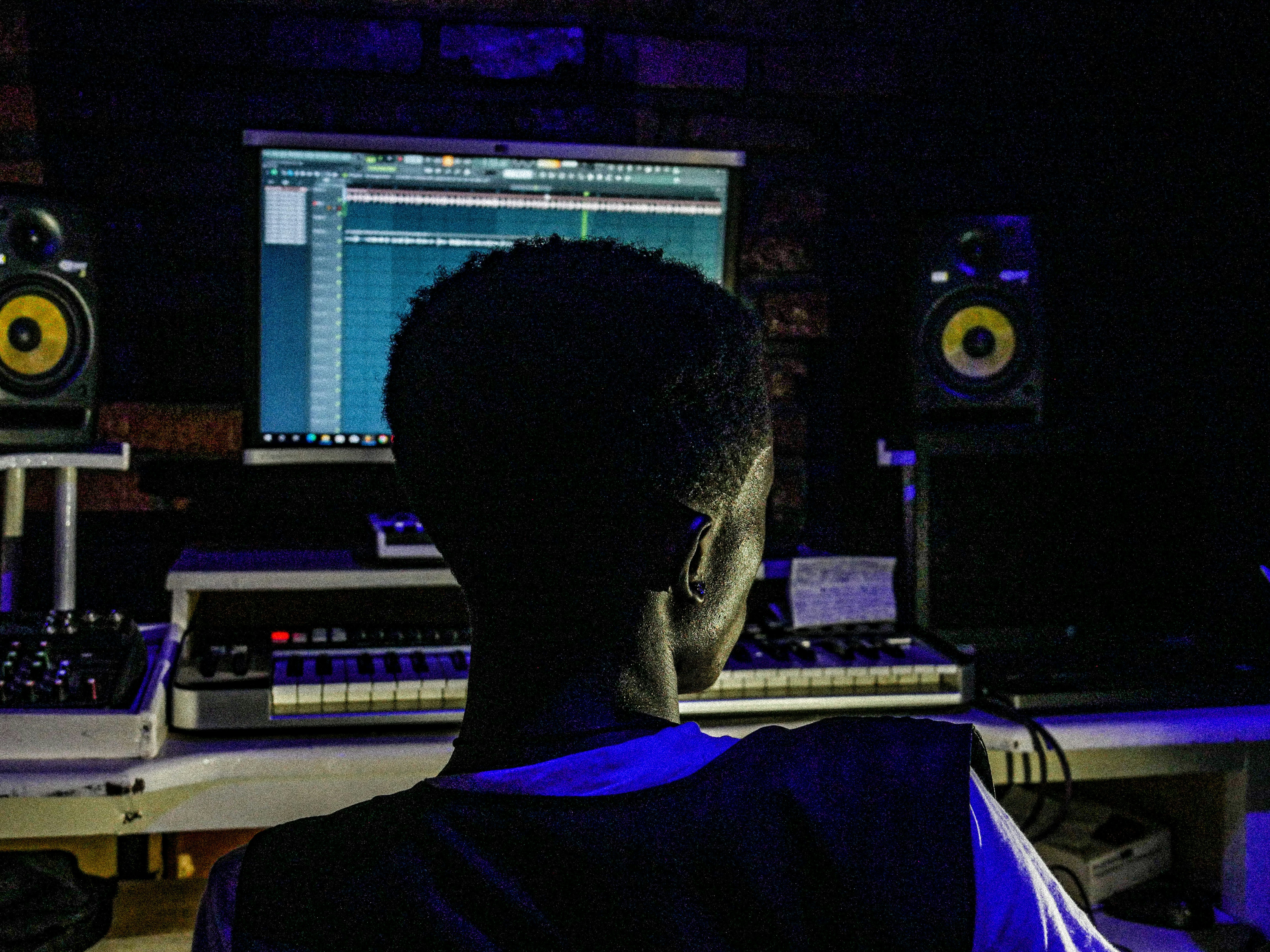 Music production desk with glowing computer screen, dark moody studio environment