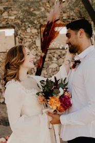 A joyful couple exchanging vows outdoors with gentle silver and white floral decorations.