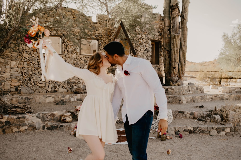 a man and a woman kissing in front of a stone building