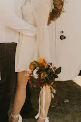 Sunlit wedding bouquet with soft sand and terracotta blooms held by a joyful bride.