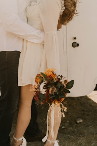 A warm, intimate photo from the engagement shoot with burnt orange and burgundy accents framing the couple smiling under soft greenery.