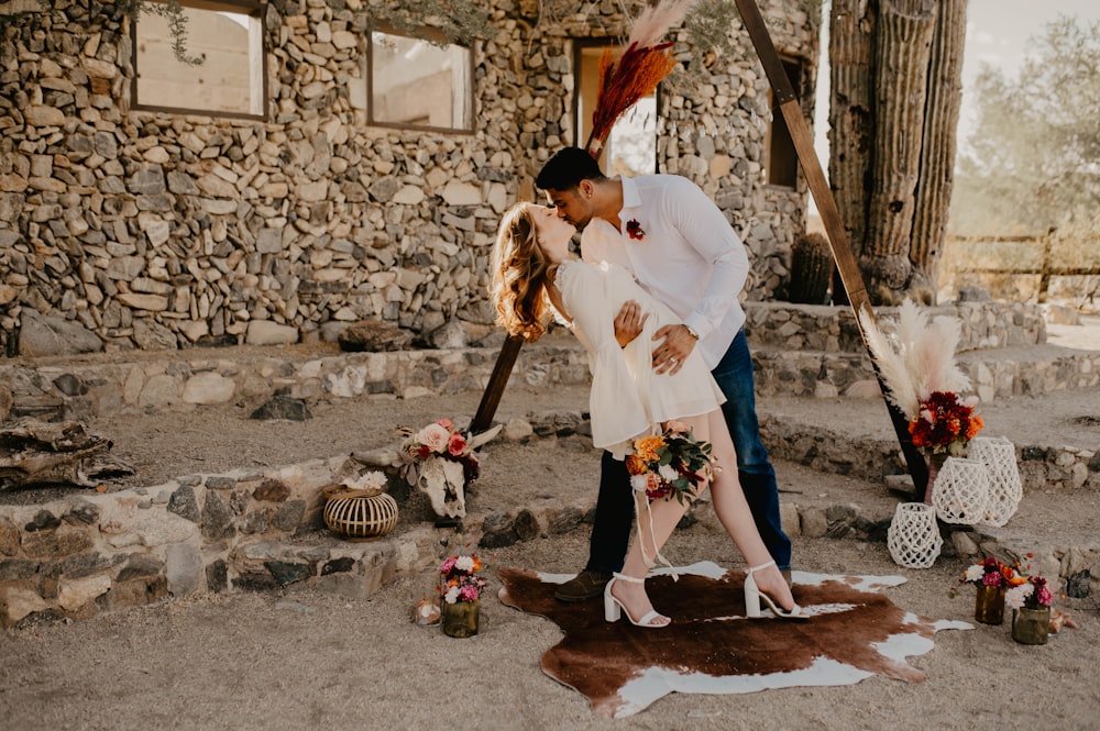 a man and woman kissing in front of a stone building