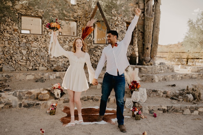A joyful couple holding hands under a floral arch at sunset.