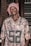 A person is wearing a camouflage-patterned Packers jersey with the number 52 prominently displayed. They have a red and white patterned headscarf wrapped around their head. The background consists of a brick wall and a set of blinds or shutters on the right side.